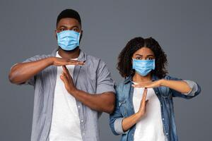 Quarantine Time Concept. Young Black Couple In Protective Medical Masks Showing Time-Out Gesture While Standing Over Light Background In Studio photo