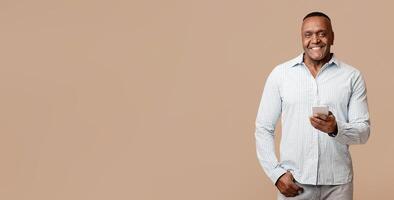 Always in touch. Handsome mature african man networking on cellphone, orange studio background photo