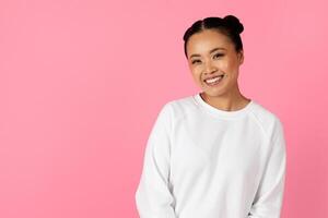 A young woman stands smiling brightly in front of a lively pink backdrop. She wears a cozy white sweatshirt, showcasing a joyful and friendly expression that adds warmth to the scene, copy space photo