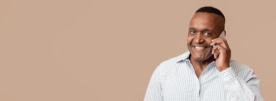 Mobile talk. Portrait of positive middle aged african american man talking on cellphone, orange studio photo