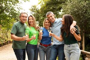 A group of five friends celebrates together in a vibrant garden, raising their glasses of wine. Laughter and camaraderie fill the air as they enjoy each other's company in a sunny atmosphere. photo
