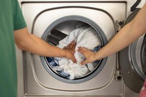 A man and woman are placing clothes into a washing machine, sharing a task in their cozy home laundry space. Their hands touch as they work together to complete the chore. photo