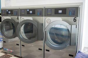 Three sleek coin-operated washing machines lined up in a tidy laundromat, featuring a bright interior with clear digital displays and spacious surroundings. photo