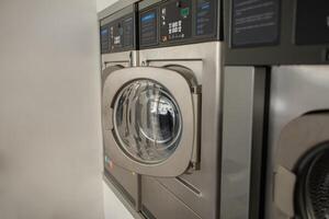 A row of sleek, stainless steel laundry machines is operational in a self-service laundromat during the late afternoon, showcasing a clean and efficient washing experience for customers. photo