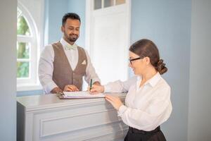 A receptionist is helping a guest with check-in at a stylish hotel lobby. The warm atmosphere and attentive service create a welcoming experience for visitors. photo