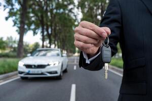 Man holds car key with a white car and trees in the background photo