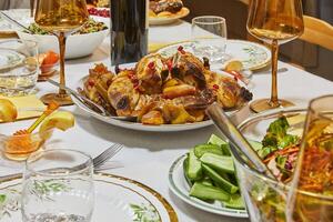 A golden roasted chicken garnished with pomegranate seeds, presented elegantly on a dining table with glasses and side dishes. photo