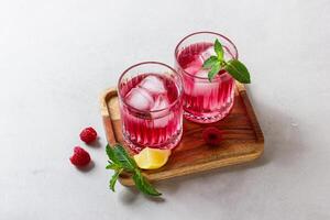 Raspberry cocktail with ice in a glass on a light background photo