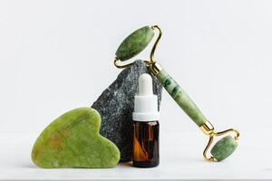 Green jade roller massager for face on white marble. photo