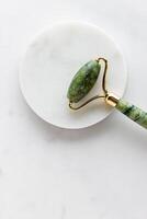 Green jade roller massager for face on white marble. photo