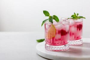 Raspberry cocktail with ice in a glass on a light background photo