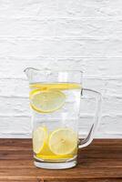 Water with lemons in jug on wooden table. photo