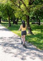 Girl rides a scooter along bicycle paths in the city in the summer. photo