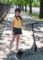 Girl rides a scooter along bicycle paths in the city in the summer. photo