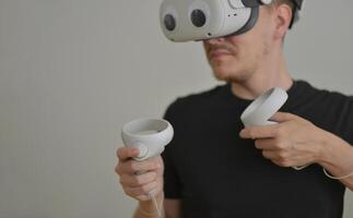 A Young Man Playing using Visual Reality Glasses with eye stickers. VR Headset Goggles Connecting Metaverse with Joysticks. Futuristic Cyberspace Technology, Virtual Digital Environment Concept photo