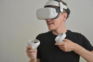 A Young Man Playing using Visual Reality Glasses with Joysticks with Copy Space. VR Headset Goggles Connecting Metaverse. Futuristic Cyberspace Technology, Virtual Digital Environment Concept photo