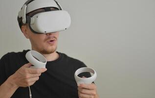 A Young Man Playing using Visual Reality Glasses with Joysticks with Copy Space. VR Headset Goggles Connecting Metaverse. Futuristic Cyberspace Technology, Virtual Digital Environment Concept photo