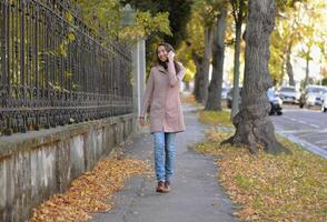 A woman talking on a phone at the street on a sunny autumn day. A woman smiles while using a mobile smartphone device photo