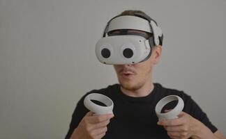 A Young Man Playing using Visual Reality Glasses with eye stickers. VR Headset Goggles Connecting Metaverse with Joysticks. Futuristic Cyberspace Technology, Virtual Digital Environment Concept photo