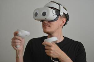 A Young Man Playing using Visual Reality Glasses with eye stickers. VR Headset Goggles Connecting Metaverse with Joysticks. Futuristic Cyberspace Technology, Virtual Digital Environment Concept photo
