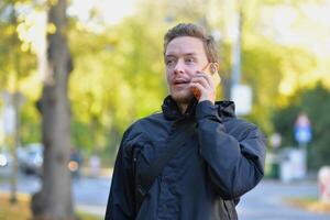 A man talking on a phone at the street on a sunny autumn day. A man uses a mobile smartphone device. Surprise, wonder and astonishment emotional expression photo