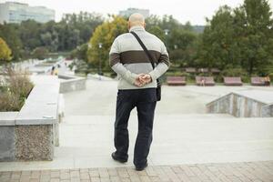 Man walks in city in summer. Pensioner in park. Man from back. Man keeps his hands behind his back. photo