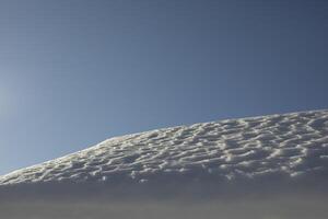 The snow on the roof. Snow and sky. Melting of the snow layer. photo