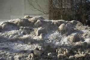 Dirty pile of snow in the city. Removing snow from the road. Dirty sand. photo