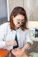 Dermatologist making a routine checkup on a senior famale patient using a binocular loupe. photo