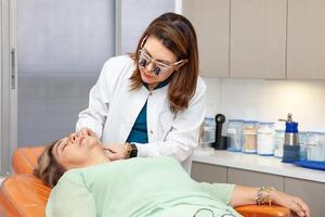 Dermatologist making a routine checkup on a senior famale patient using a binocular loupe. photo