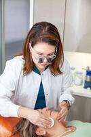 Dermatologist making a routine checkup on a senior famale patient using a binocular loupe. photo