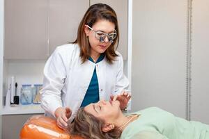 Dermatologist making a routine checkup on a senior famale patient using a binocular loupe. photo