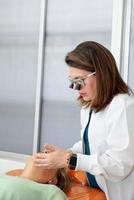 Dermatologist making a routine checkup on a senior famale patient using a binocular loupe. photo