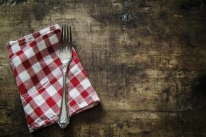 A fork and knife on a table with a red and white checkered napkin photo