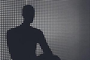 Silhouette of a man sitting on a chair in front of a wall with dots photo