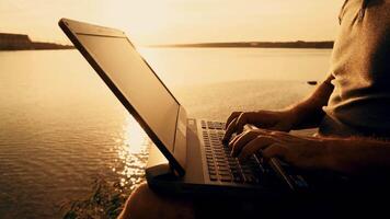 Man's hands using laptop computer on top of a hill by the river. Beautiful summer sunset video