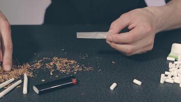 Man in Black Clothing is Rolling a Hand Made Cigarette Using Papers, Filters and Tobacco. A Way to Save on Tobacco Products. Tobacco Product Economy Concept video