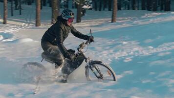 Cyclist in Black Clothes, Helmet and Snow Glasses Riding on Electric Bike in the Snow in Winter Forest. E-Bike Riding and Drifting at Cold Sunny Day - Slow Motion video