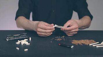 Man in Black Clothing is Rolling a Hand Made Cigarette Using Papers, Filters and Tobacco. A Way to Save on Tobacco Products. Tobacco Product Economy Concept video