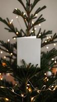 Blank white greeting card mockup between Christmas tree branches. Warm and cozy aesthetic christmas scene background with a blank paper with copy space. photo