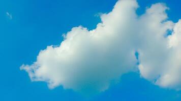 A single, fluffy white cloud drifts across a clear blue sky. The cloud is small and delicate, with soft, rounded edges. The sky is a deep, vibrant blue, with no other clouds in sight. photo