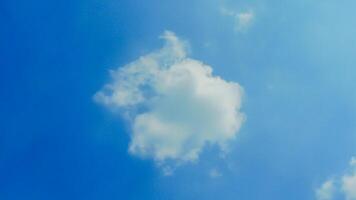 A single, fluffy white cloud drifts across a clear blue sky. The cloud is small and delicate, with soft, rounded edges. The sky is a deep, vibrant blue, with no other clouds in sight. photo
