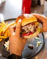 Man holding tasty hamburger with french fries on restaurant table photo