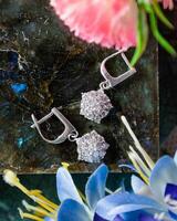 Pair of sparkling silver earrings with diamonds resting on stone surface photo