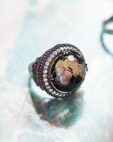Silver ring with large stone and small emerald and ruby gemstones is lying on the table photo