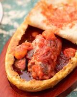 Traditional tajik meat dish with vegetables and tomato sauce in bread on wooden board photo