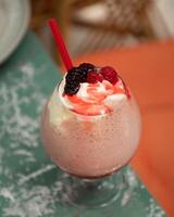 Delicious pink cocktail topped with whipped cream, berries, and red straw is sitting on a table photo