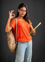 Beautiful young girl with a backpack standing and holding a notebook, posing on a grey background. photo
