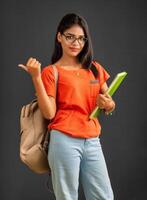 Beautiful young girl with a backpack standing and holding a notebook, posing on a grey background. photo
