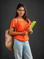 Beautiful young girl with a backpack standing and holding a notebook, posing on a grey background. photo